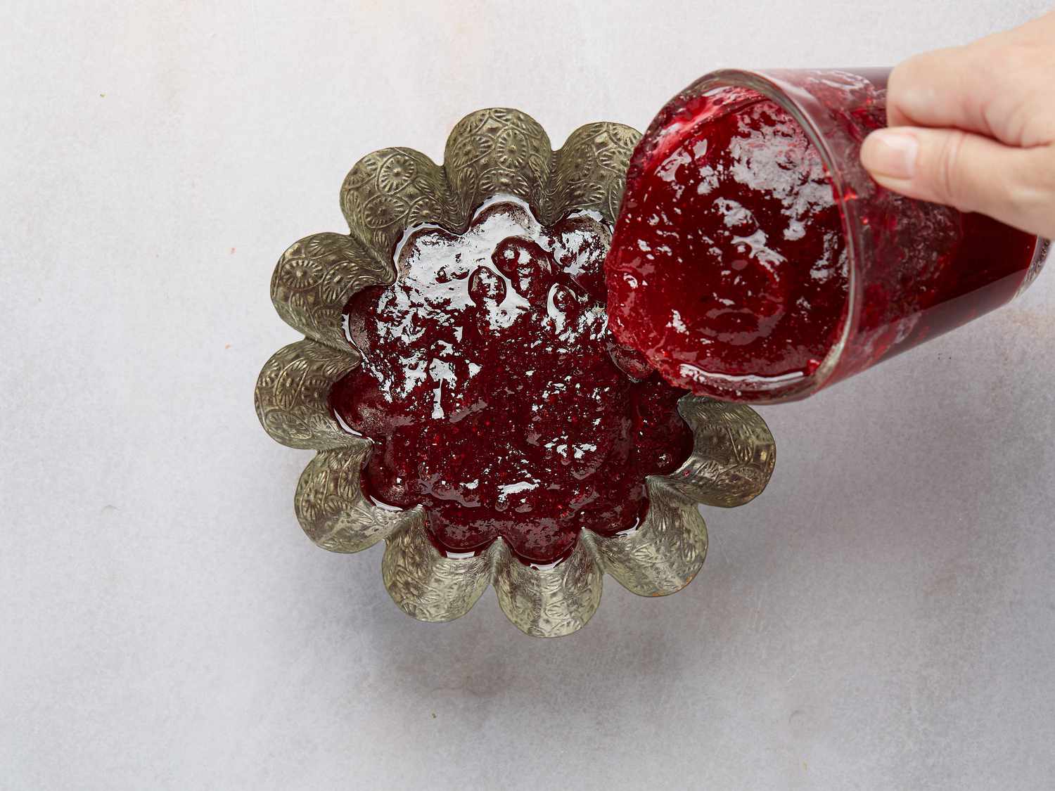Hand pouring jellied cranberry sauce from glass measuring cup into metal mold