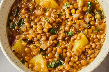 A bowl of Lebanese brown lentil soup with visible chunks of vegetables and garnished herbs