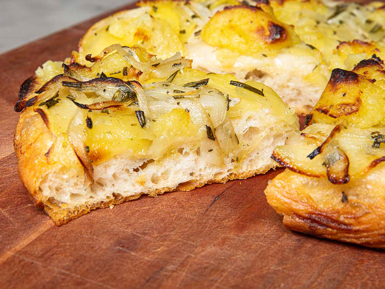 A side view of a slice of potato pizza showing off the texture of the cooked dough and toppings.