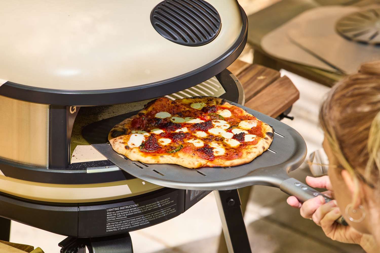 A person removes a pizza cooked in the Gozney ARC XL Compact Pizza Oven