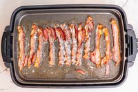 An electric griddle filled with bacon cooking