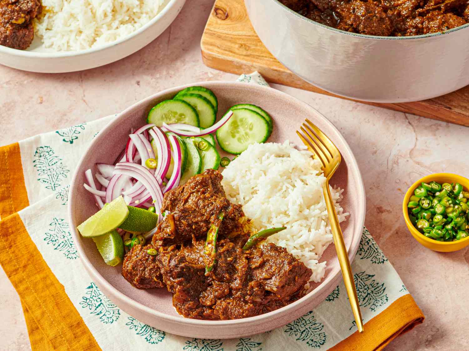 A plate with rice beef curry cucumber slices lime wedge and red onions served with a fork
