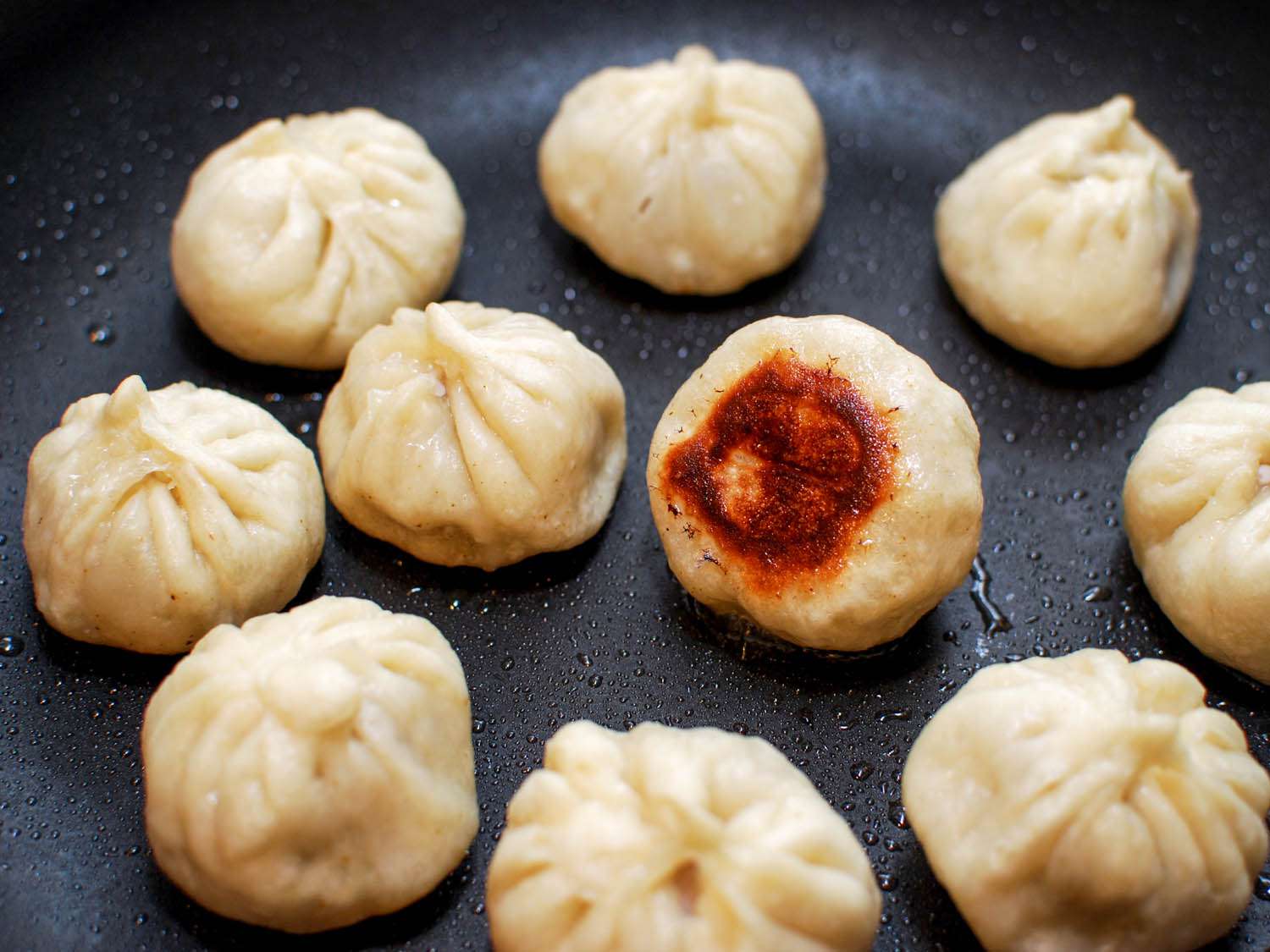 One of the sheng jian bao is turned over to reveal a crispy, deeply browned bottom.