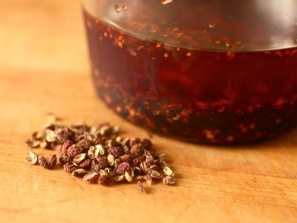 Closeup of roasted Sichuan peppercorns and a jar of roasted chile oil.