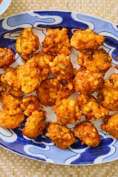Fritters on a blue and white printed plate, on a bamboo mat. Glass of blue water, and red chili sauce on the side 