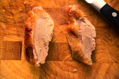 Two slices of duck on a wooden cutting board.