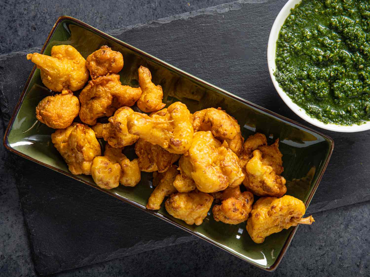 Cauliflower pakoras next to a green chutney sauce.