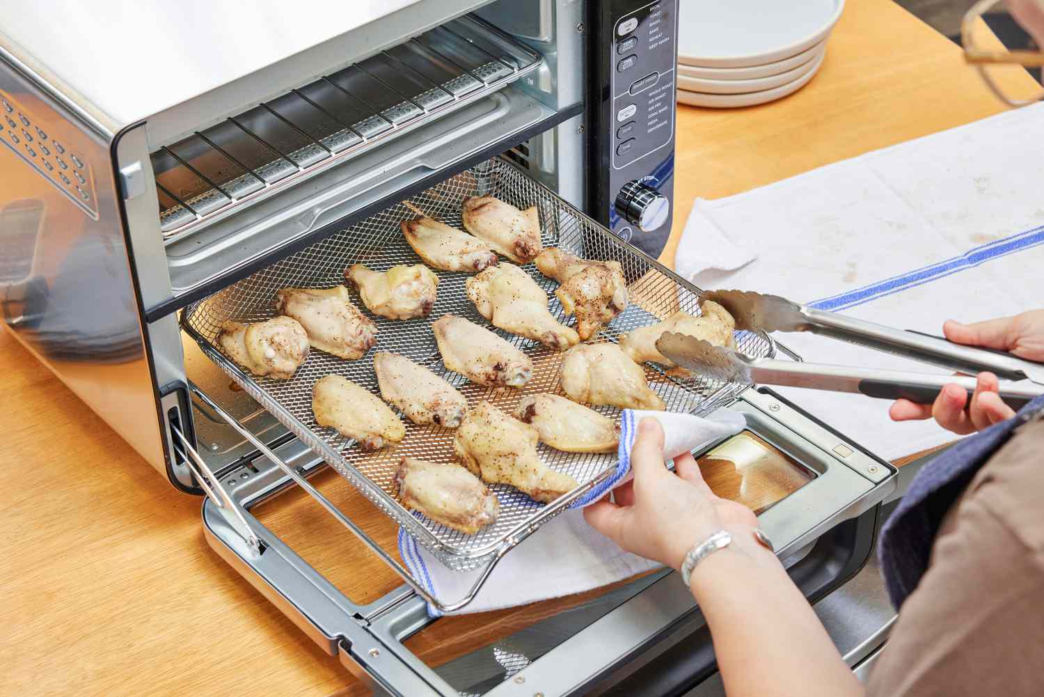 A person using tongs to flip chicken cooking in the Breville the Joule Oven Air Fryer Pro