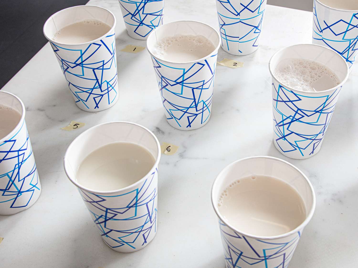 Several paper cups with oat milk placed on a marble table