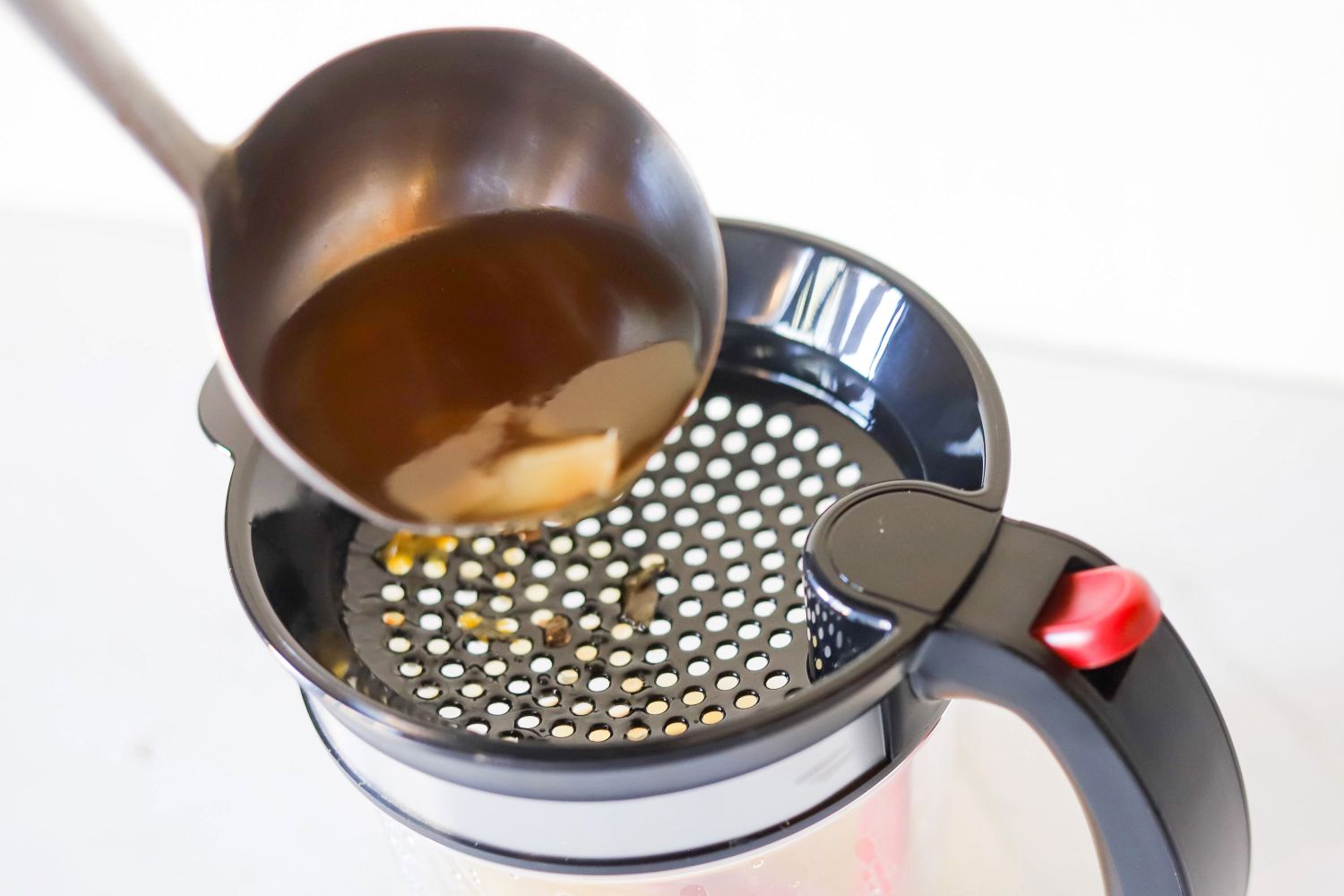 A ladle pouring liquid through a strainer into a container