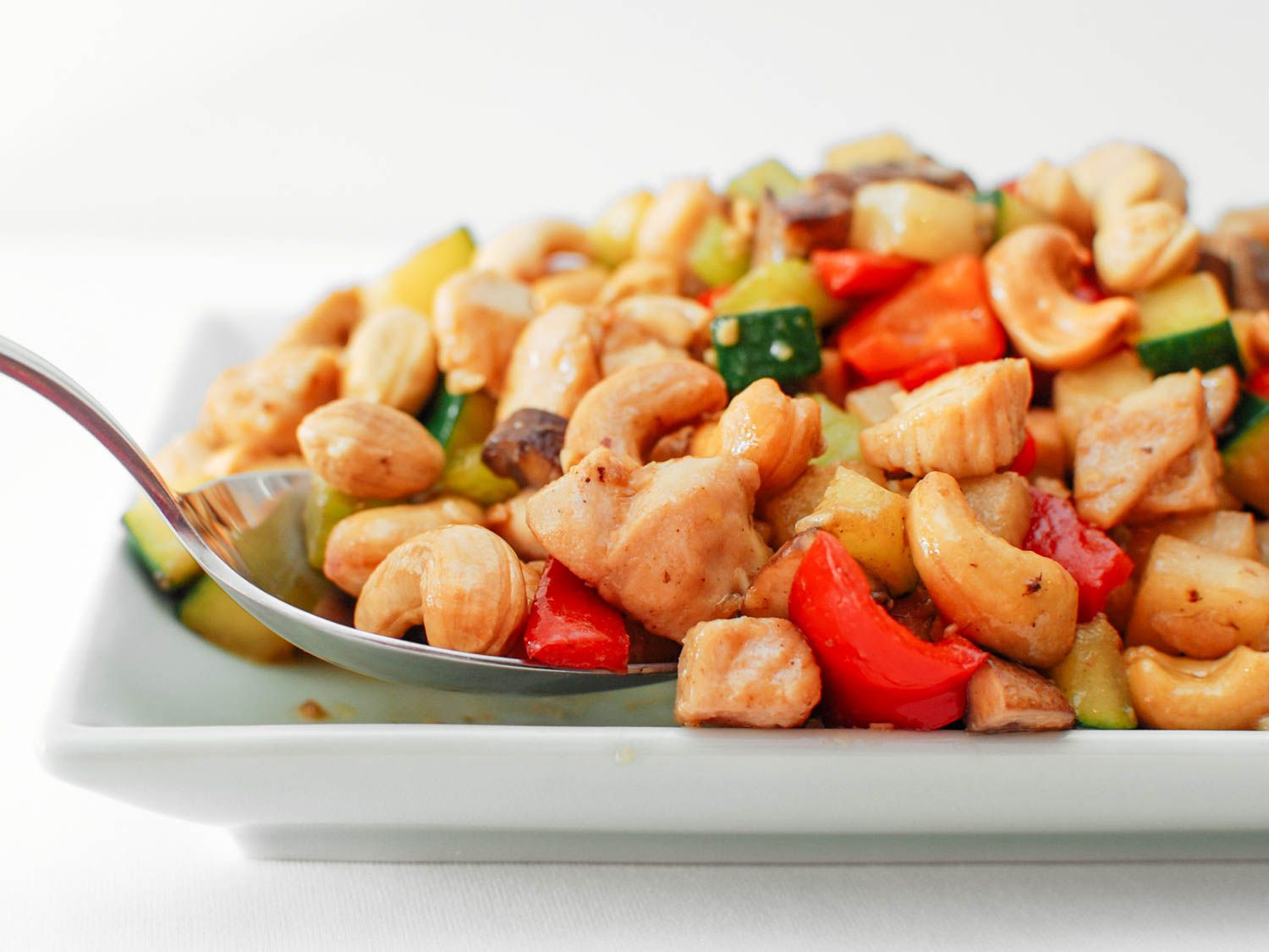 A dish of cashew chicken ding on a white plate with a serving spoon.
