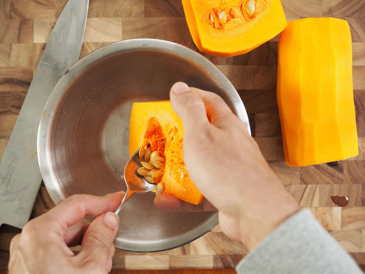 A pair of hands removing the seeds from the body of a butternut squash with a spoon.