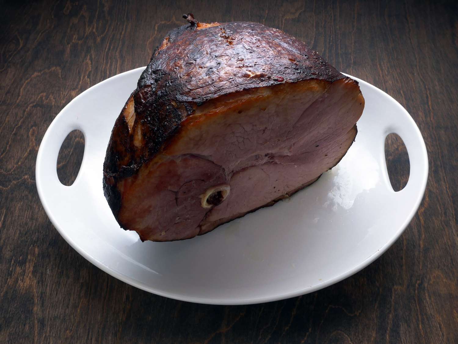 D'artagnan bone-in ham on a white platter on a wooden surface