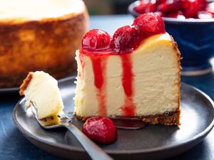A slice of epic New York Cheesecake on a plate, topped with cherry sauce. 