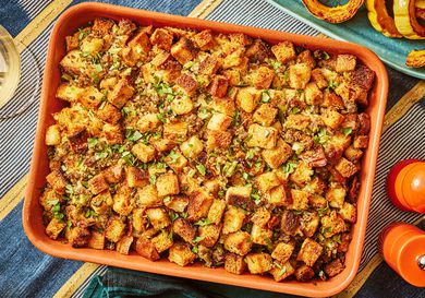 sausage and sage stuffing in orange baking dish, on a thanksgiving table, with roasted squash to the side. 