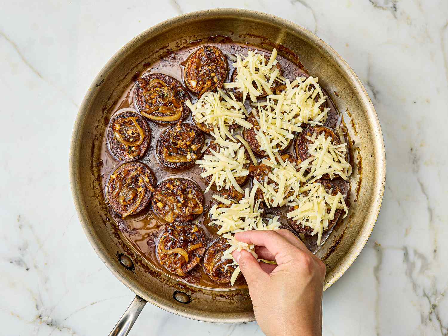 Pan of cooked onions in broth hand adding grated cheese on top