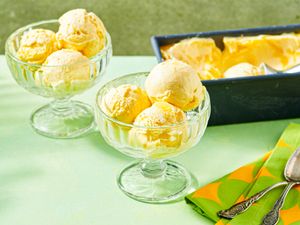 Scoops of mango ice cream in glass bowls with an ice cream tub in the background
