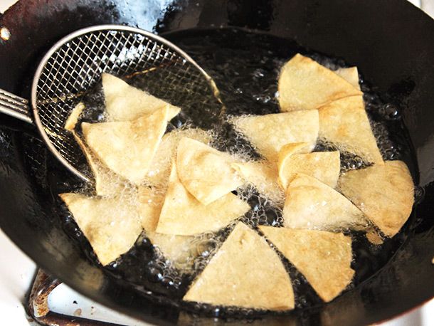 Tortilla chips frying in a wok are stirred with a spider.