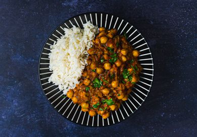 Channa masala and white rice on a blue plate decorated with white lines. The plate is on a dark blue surface.