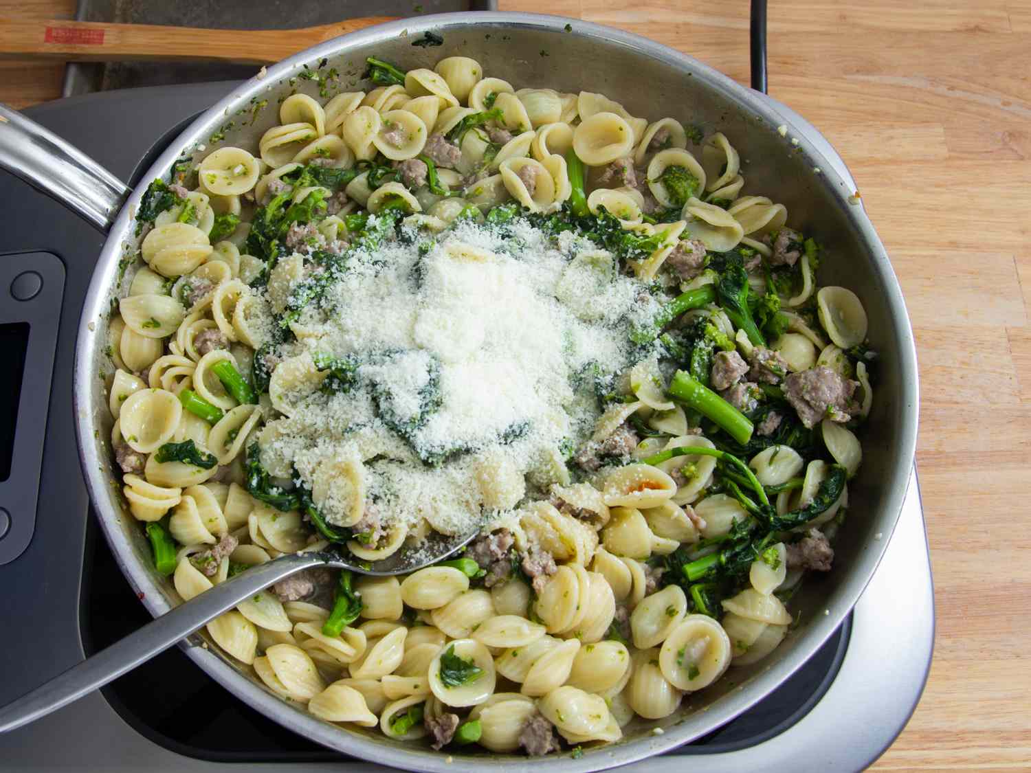 Grated Pecorino added to a skillet of orecchiette with sausage and broccoli rabe.