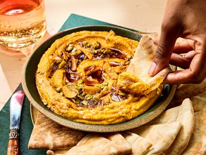 A bowl of sweet potato pepita dip with a person dipping a piece of flatbread