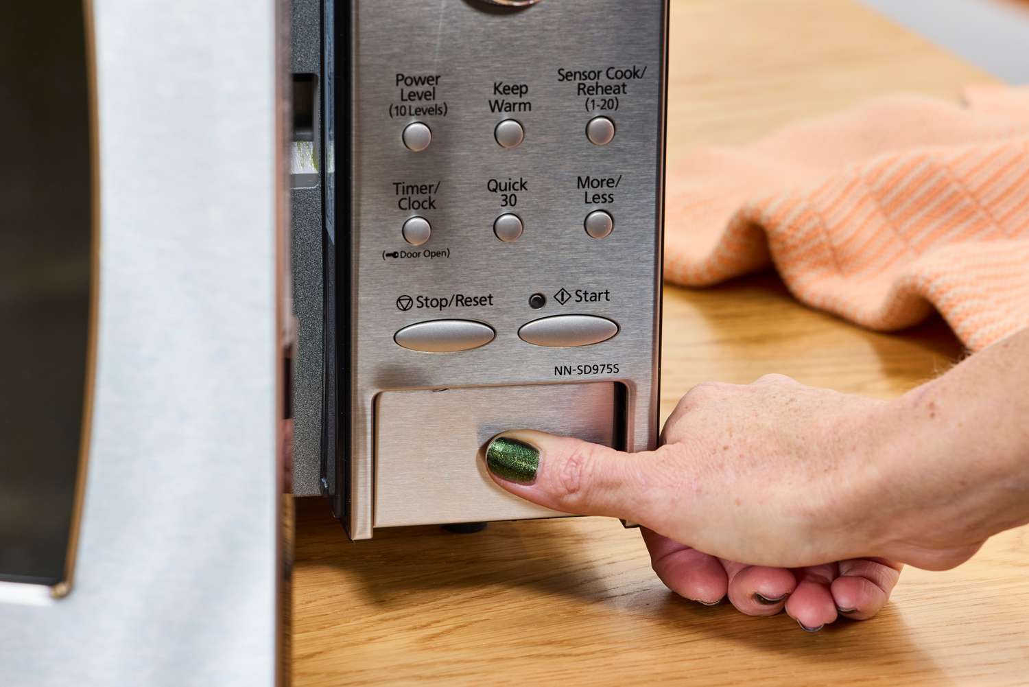 A hand pressing a button on the Panasonic - 2.2 Cu. Ft. 1250 Watt SD987SA Full-Size Microwave with Inverter