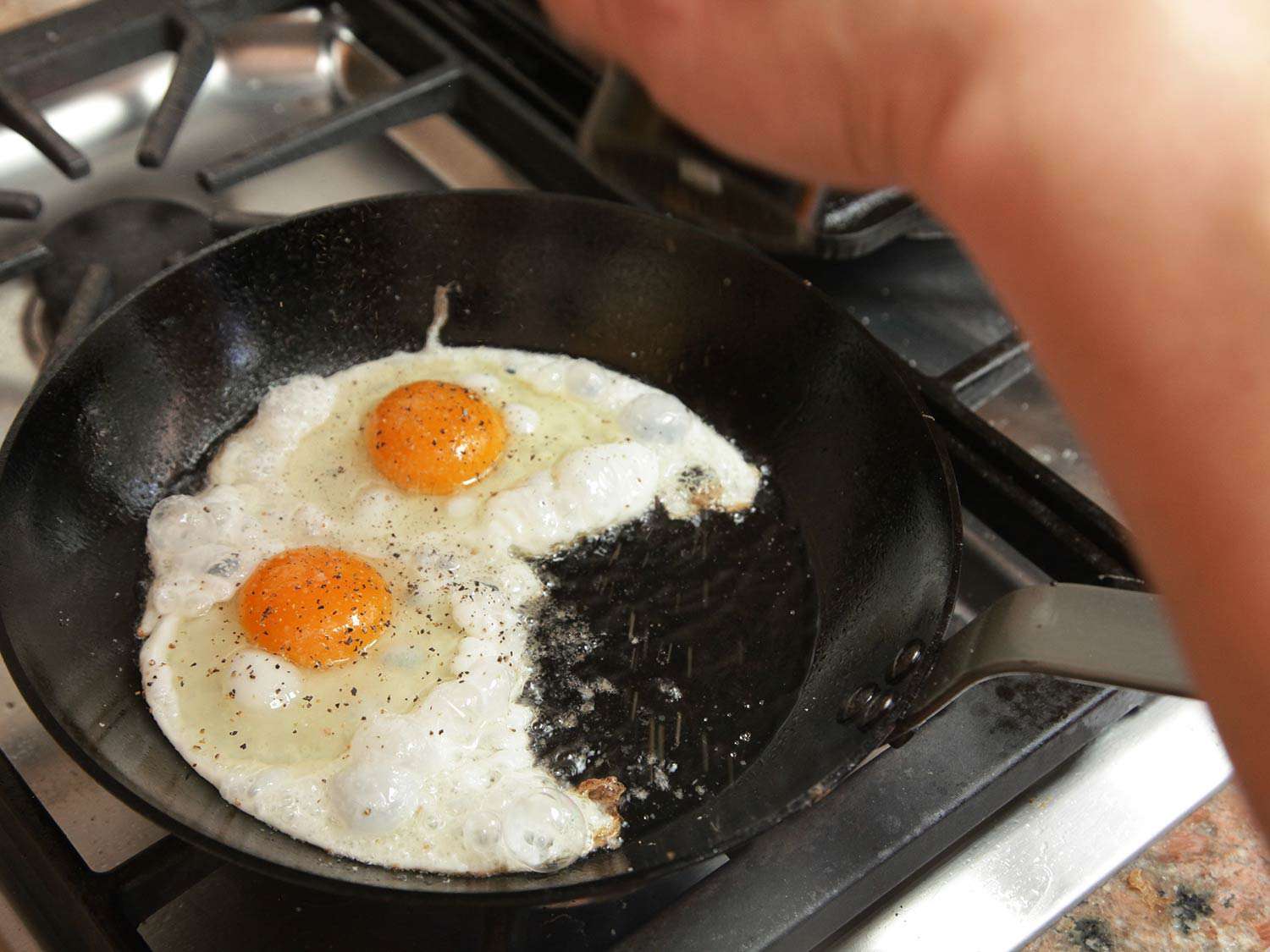 Two eggs frying in hot oil in a skillet. 