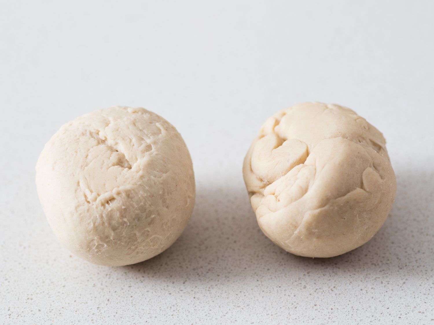 Two balls of rolled dough for homemade bagels, one smoother than the other