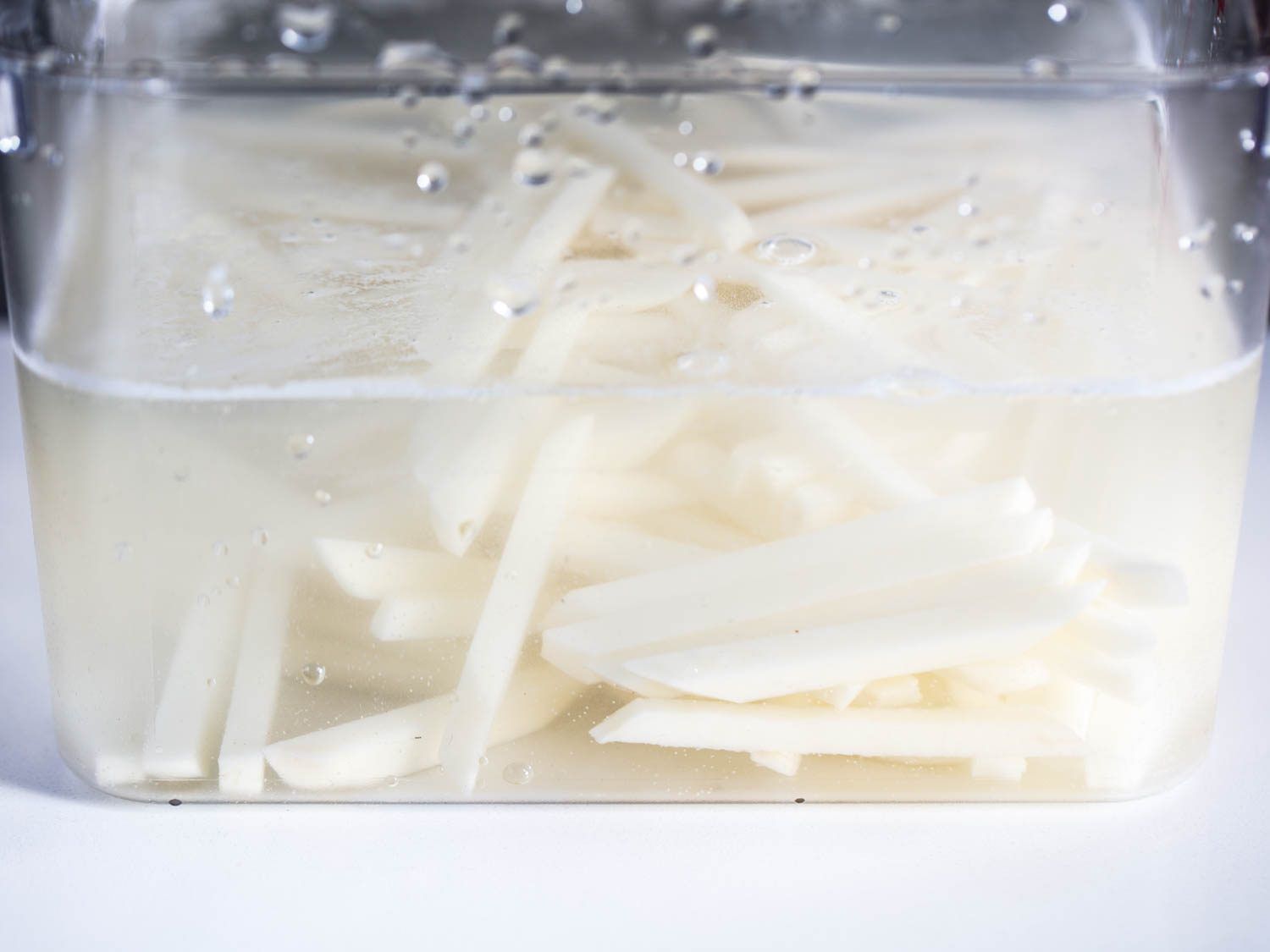 Raw potato sticks for French fries, soaking in a tub of cold water.