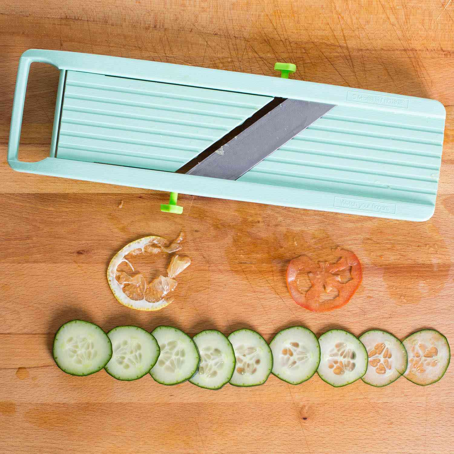 Slices of cucumber and a mangled slice of lemon and tomato next to the Benriner Mandoline
