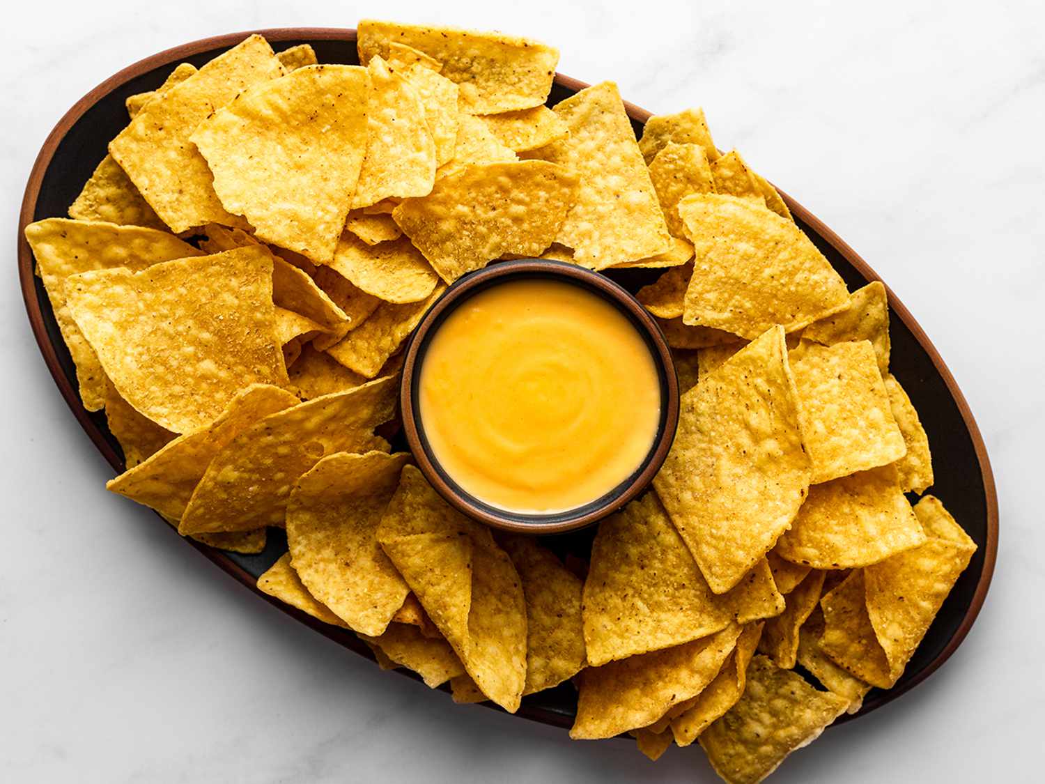 Nacho cheese sauce in a small bowl in the center of a platter, surrounded by tortilla chips.