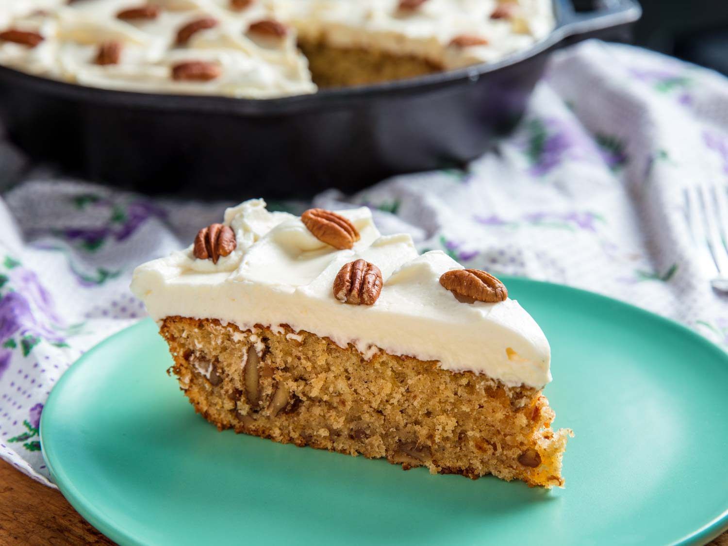 Slice of hummingbird cake topped with pecans and cream cheese frosting