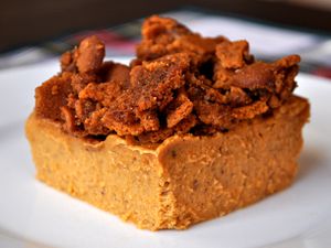 Closeup of a slice of pumpkin custard with cookie crumble topping, served on a white plate.