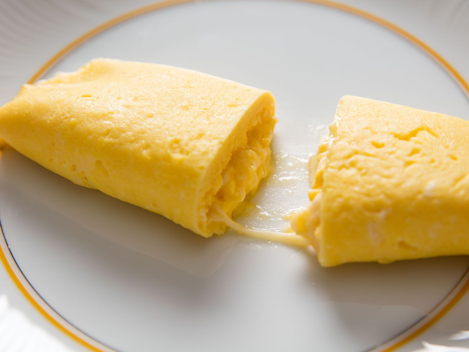 A French omelette with cheese in the middle, cut open on a white plate.