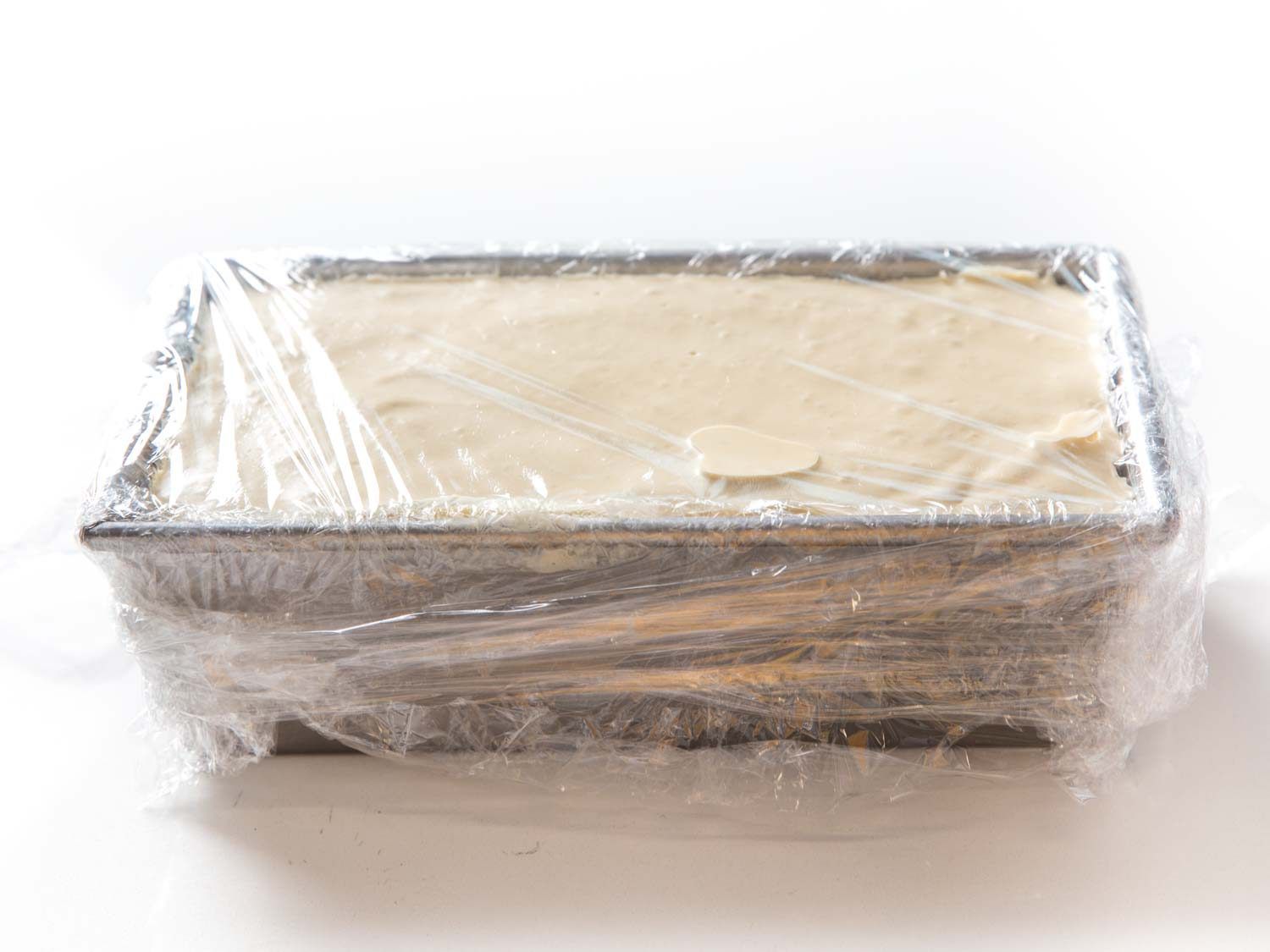 A loaf of semifreddo fully wrapped in plastic wrap. 