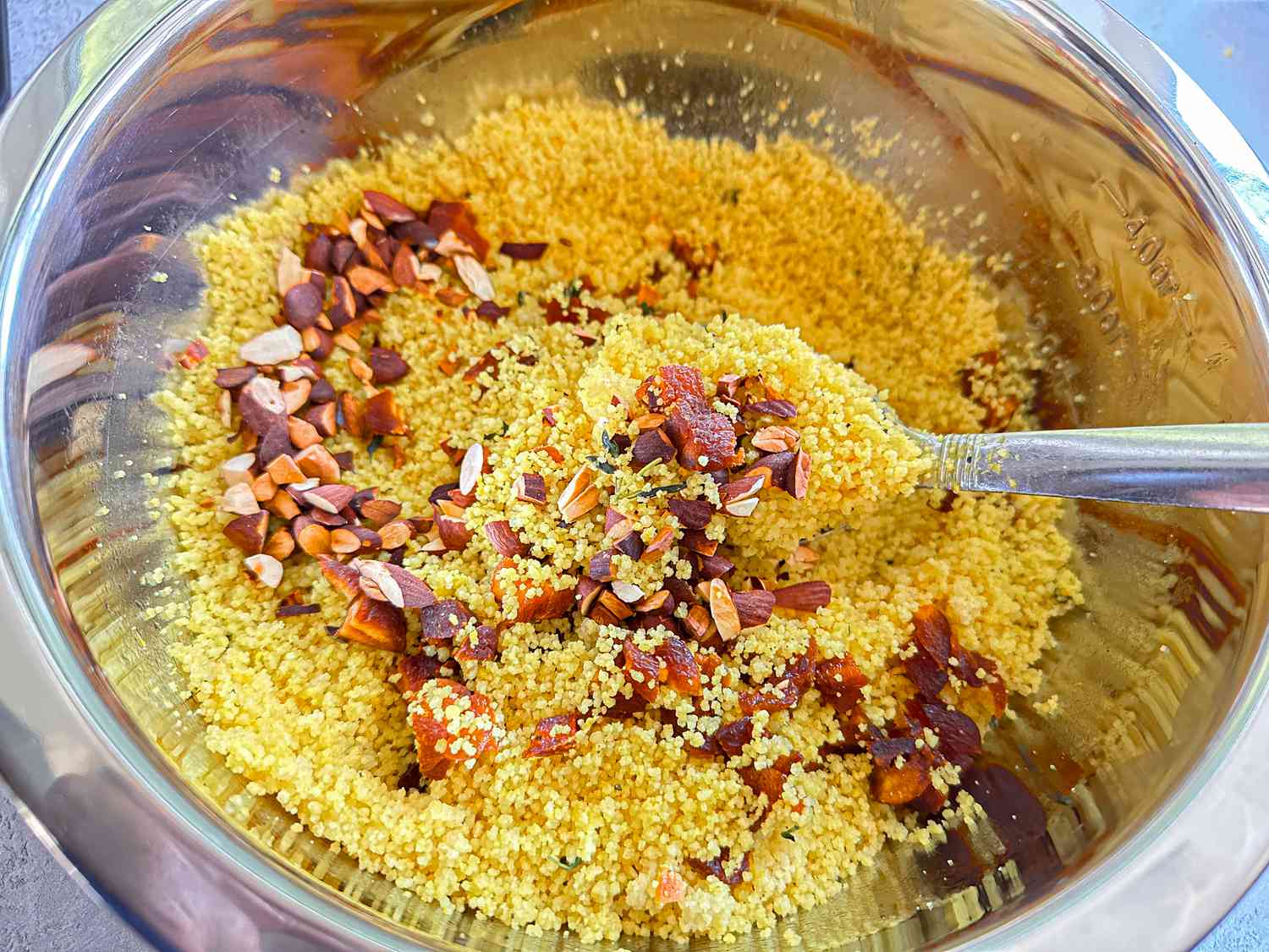 Bowl of couscous mixed with chopped almonds and spices, preparation in progress