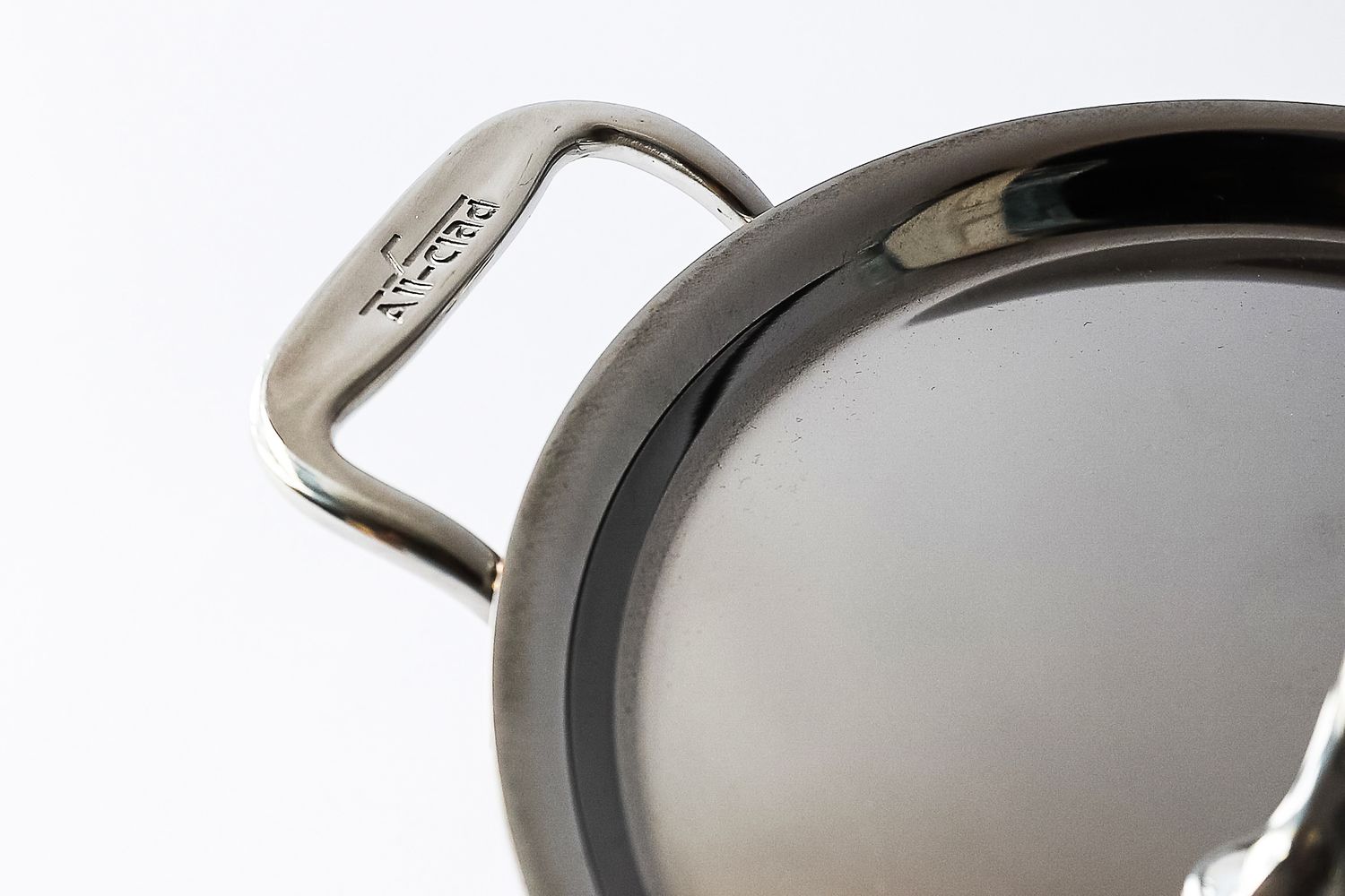 A closeup of a metal saucepan handle with the brand name AllClad engraved