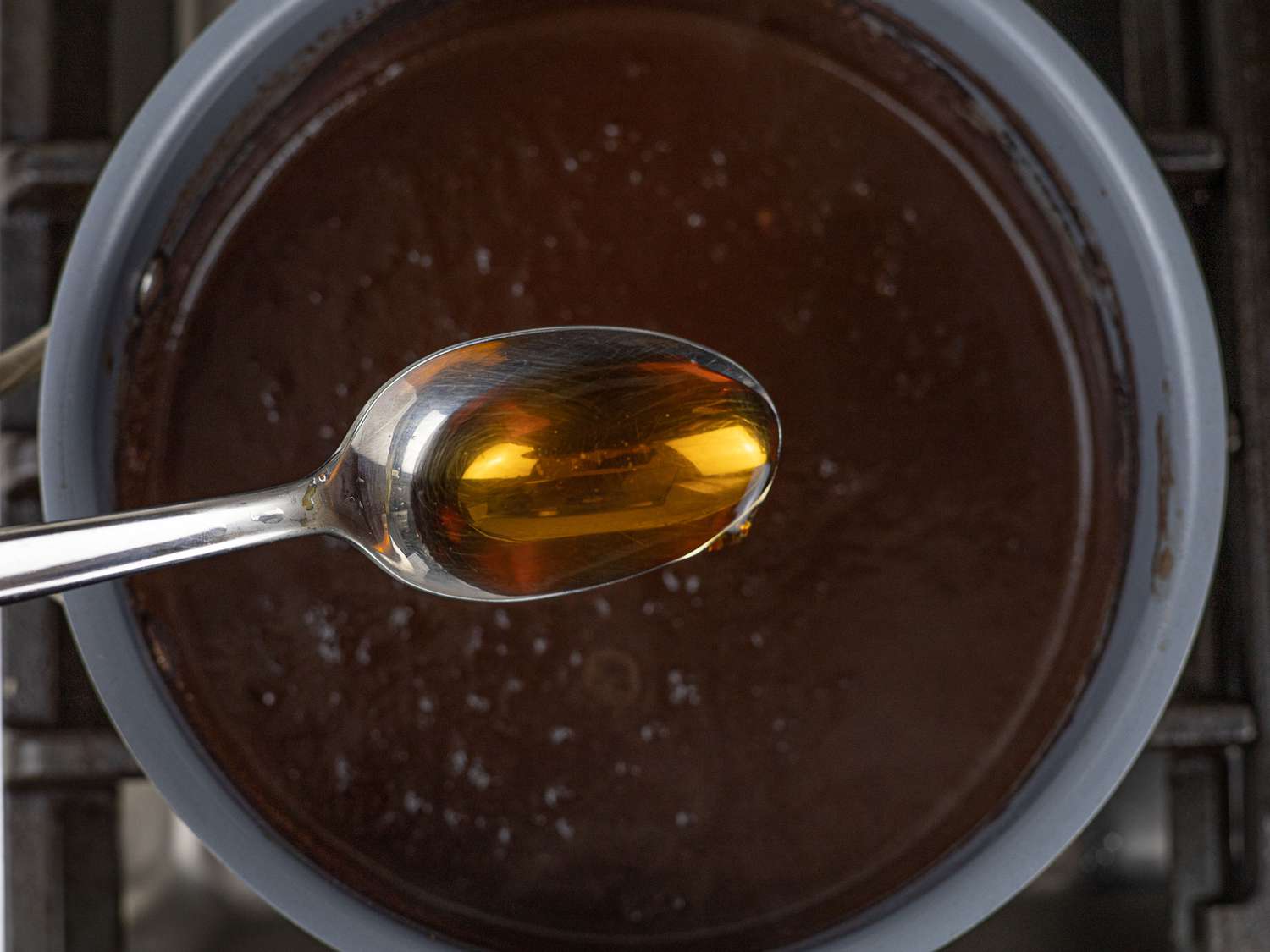 Spoon with fish sauce held over saucepan with pork blood sauce