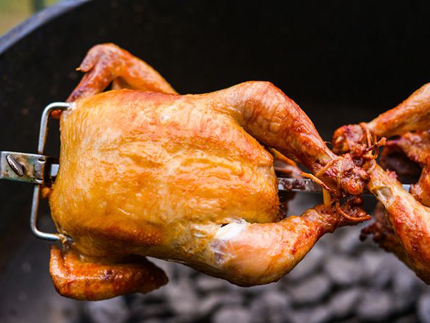 A rotisserie chicken turns on a spit over a charcoal fire.