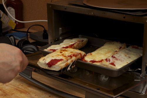 French bread pizzas are removed from a toaster oven.
