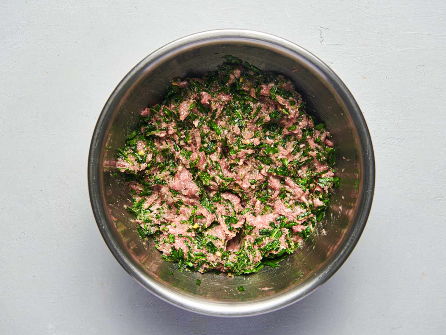 Oil, chives, ground park, salt, sugar, rice wine, pork stock or water, and ginger thoroughly combined inside a medium bowl.