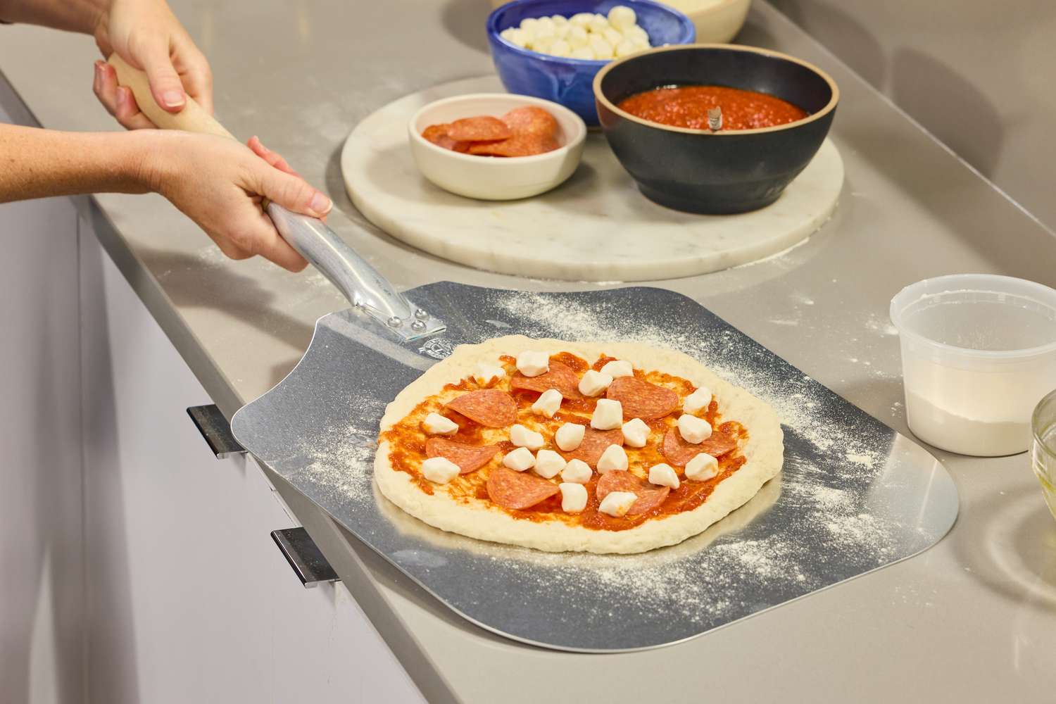A person prepares to cook a pizza assembled on the American Metalcraft Aluminum Pizza Peel