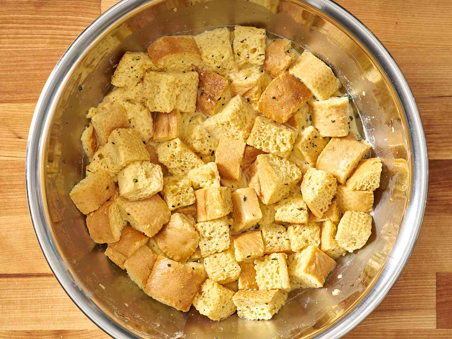 Dried bread cubes in a mixing bowl after soaking in strata custard mixture