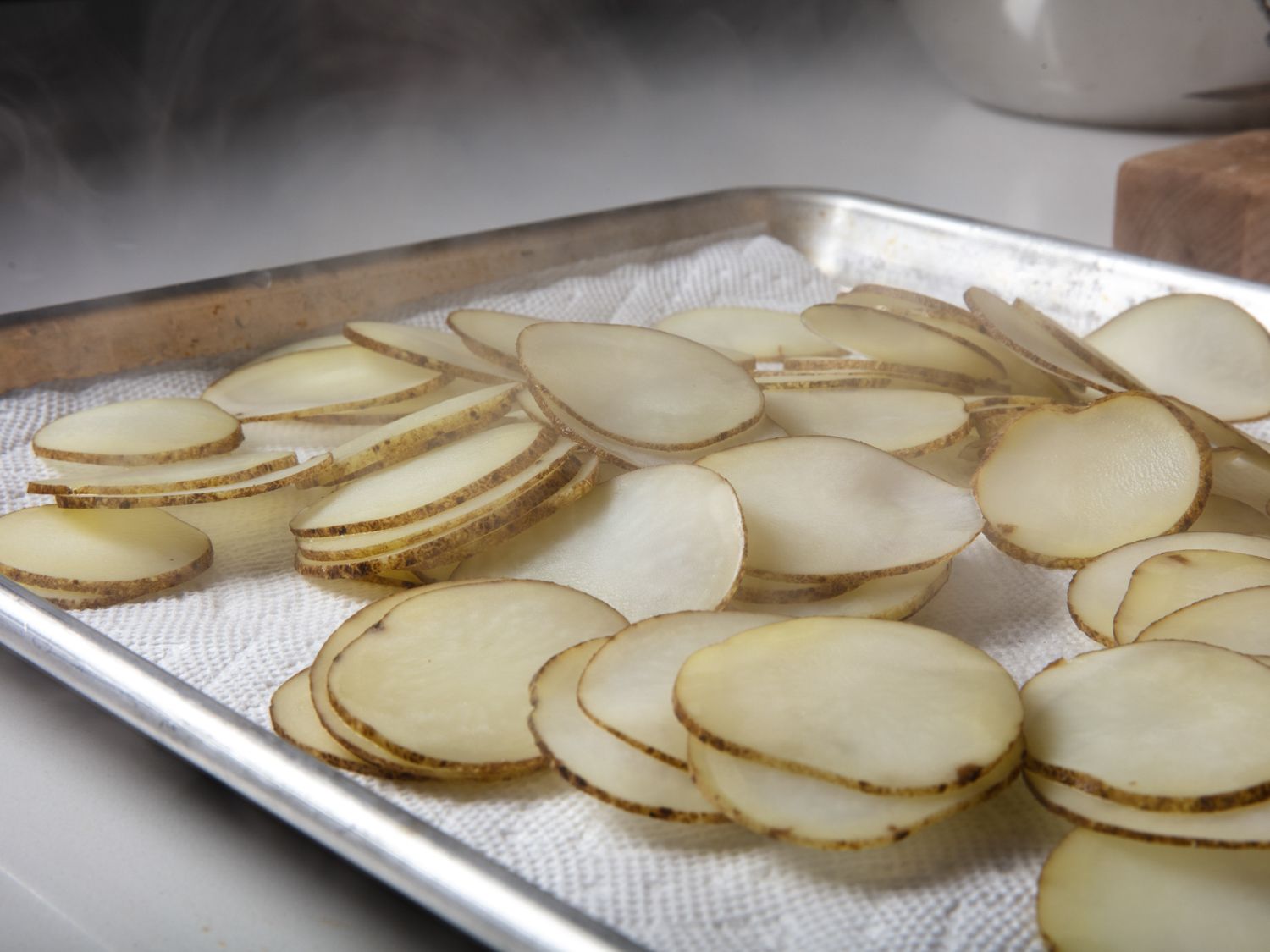 Steaming blanched potatoes drying on a paper towel set inside of a half sheet pan.