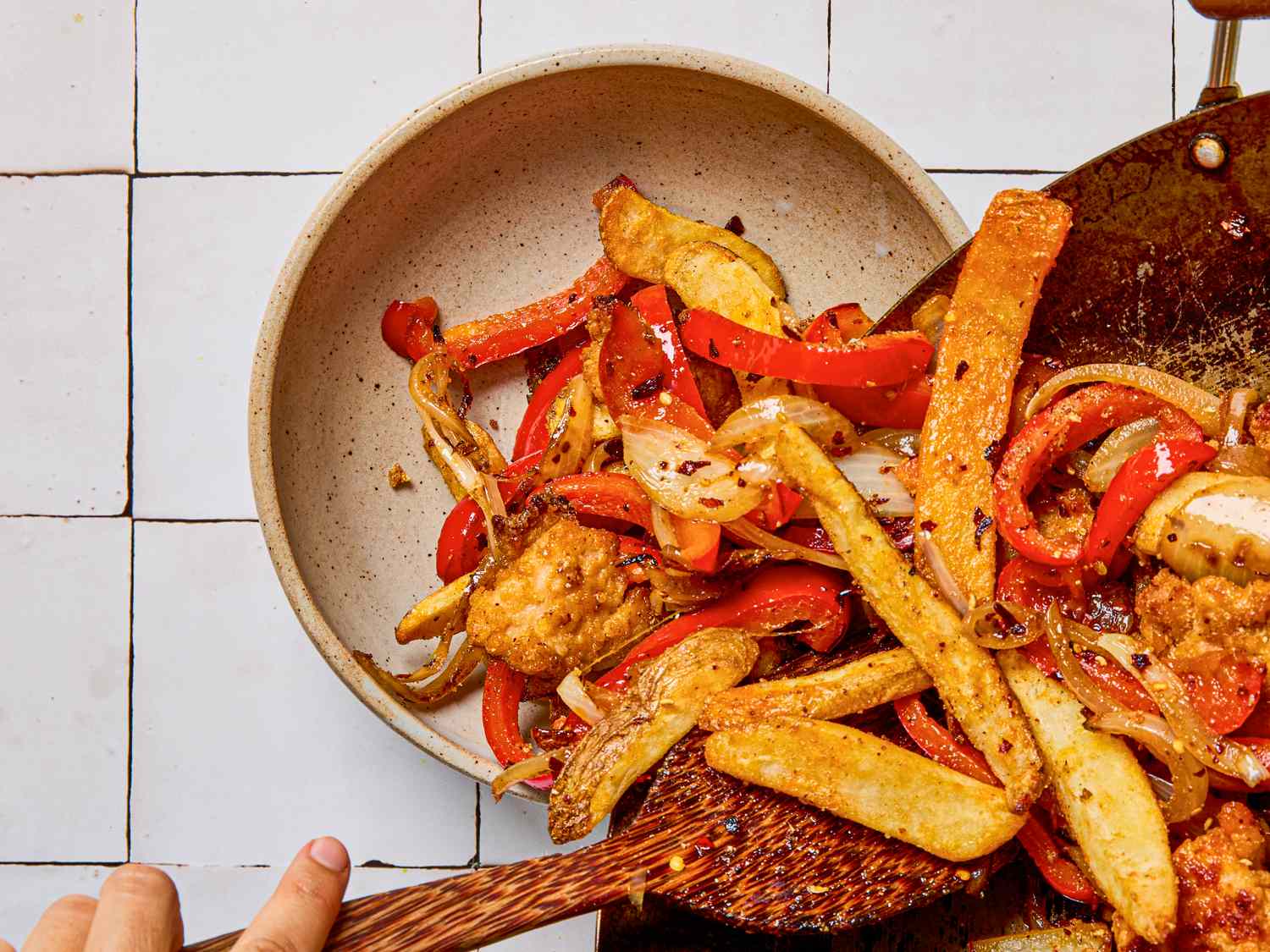 A dish with fried ingredients including peppers and potatoes being served from a pan