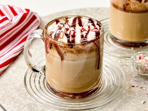 A mug of coffee topped with whipped cream chocolate drizzle and crushed peppermint candy