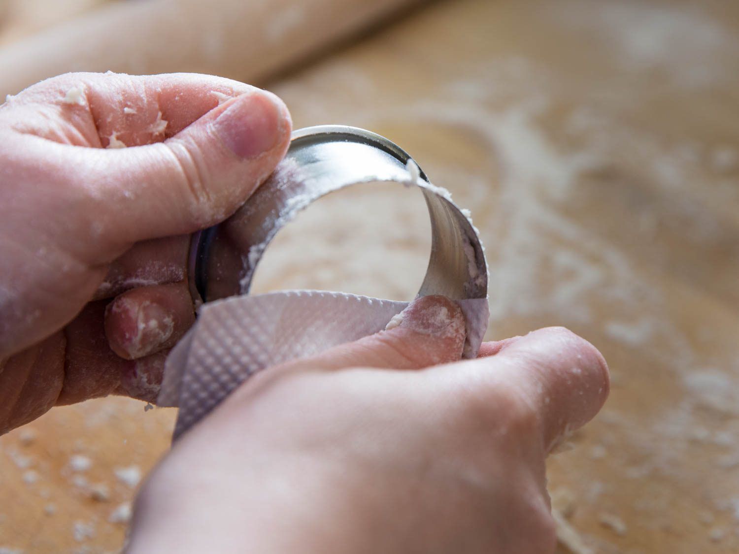 Wiping off dough on a round biscuit cutter.