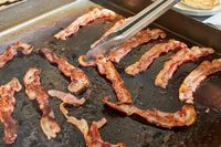 Bacon is cooked on the Blackstone 1554 Cooking 4 Burner Flat Top Gas Grill