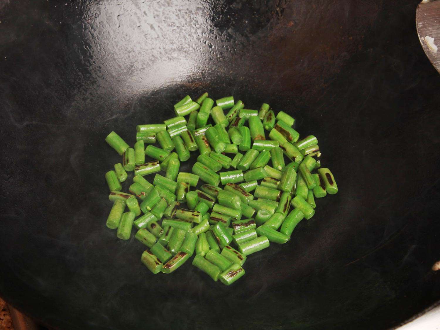 Green bean segments are seared in the wok until charred and blistered.