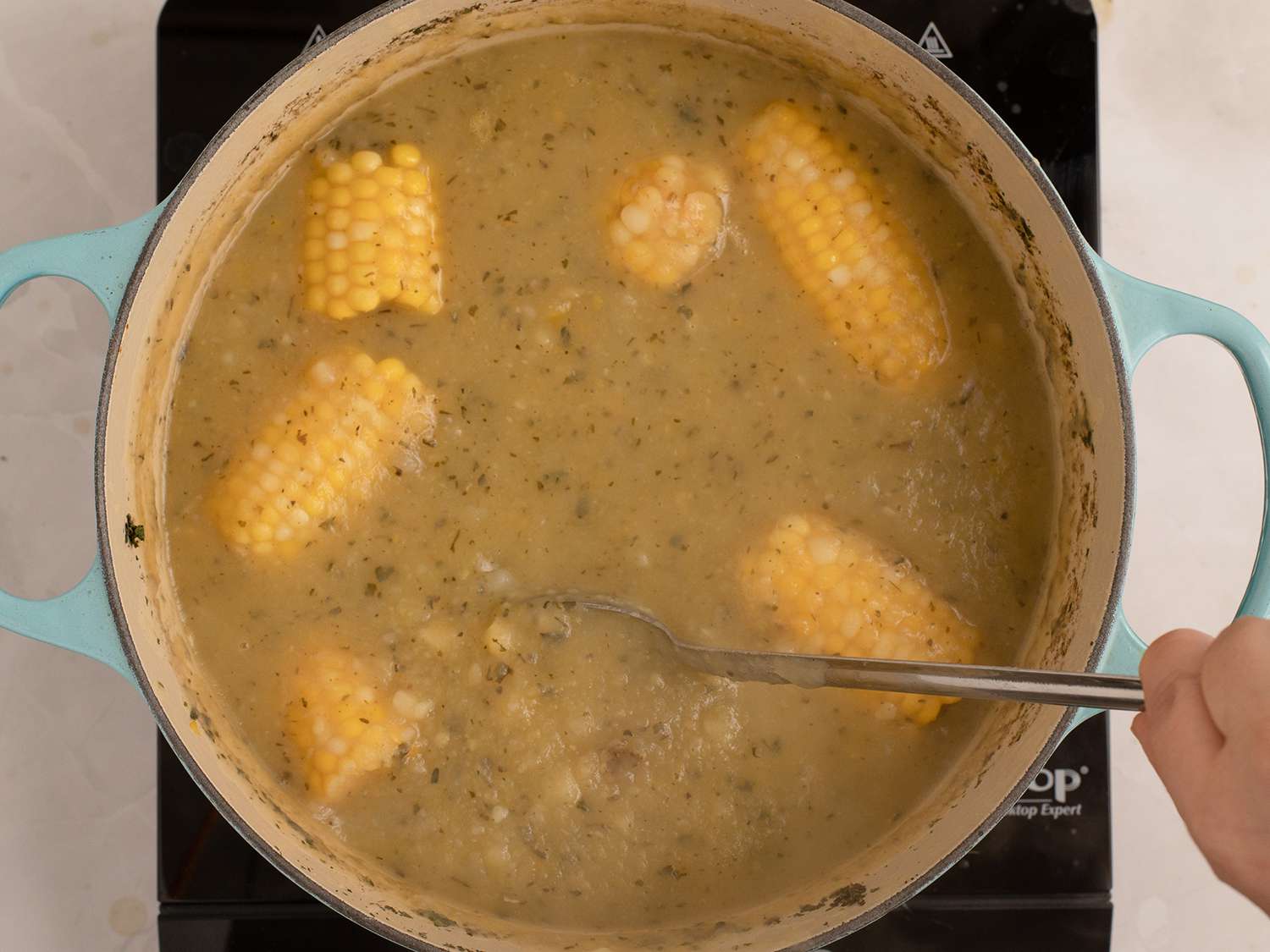 A pot of soup with corn cobs.